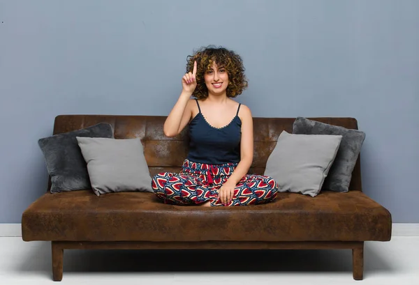 楽しそうに笑っている若い女性がソファに座っている空間をコピーするために片手で上を向いて — ストック写真