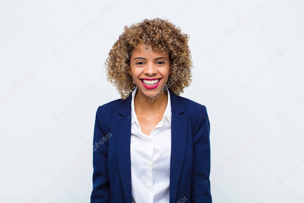 young woman african american with a big, friendly, carefree smile, looking positive, relaxed and happy, chilling against flat wall