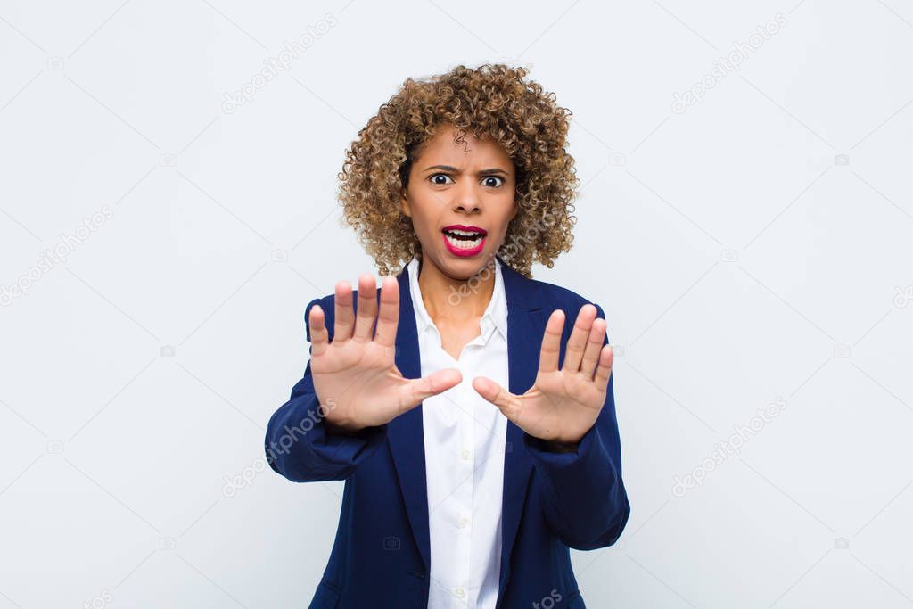 young woman african american feeling terrified, backing off and screaming in horror and panic, reacting to a nightmare against flat wall