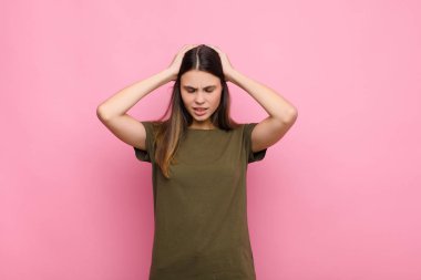 Genç, güzel bir kadın kendini stresli ve hayal kırıklığına uğramış hissediyor. Eli kolu bağlı, yorgun, mutsuz ve pembe duvarda migreni olan bir kadın.