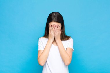 Genç, güzel bir kadın üzgün, hayal kırıklığına uğramış, gergin ve depresif, yüzünü iki eliyle kapatmış, mavi duvara karşı ağlıyor.