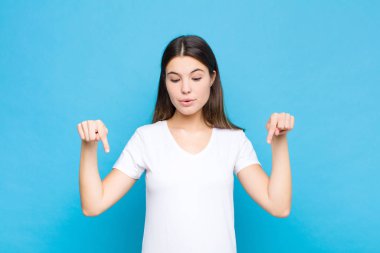Genç, güzel bir kadın şok olmuş, ağzı açık ve şaşkın, mavi duvara bakıyor ve onu işaret ediyor.