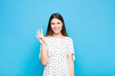 Genç, güzel bir kadın gülümsüyor ve arkadaş canlısı görünüyor. Dört ya da dört numarayı gösteriyor. Elleri önde, mavi duvara doğru sayıyor.