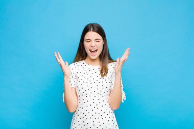 Genç ve güzel bir kadın öfkeyle bağırıyor, stresli hissediyor ve ellerini havaya kaldırıp neden mavi duvara yaslandığımı söylüyor.