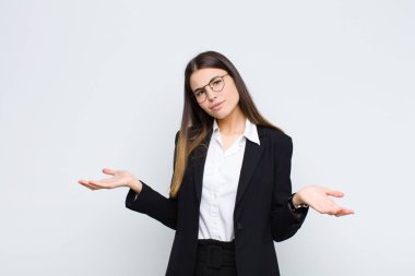 Genç iş kadını şaşkın, şaşkın ve stresli görünüyor, farklı seçenekler arasında merak ediyor, beyaz duvara karşı kendini güvensiz hissediyor