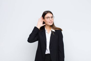 Genç iş kadını gülümsüyor, tuhaf bir şekilde yan tarafa bakıyor, dedikoduları dinlemeye çalışıyor ya da beyaz duvara karşı bir sırrı duymaya çalışıyor.