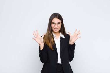 Genç iş kadını gülümsüyor ve arkadaş canlısı görünüyor, onuncu ya da onuncu numarayı gösteriyor, beyaz duvara doğru sayıyor.