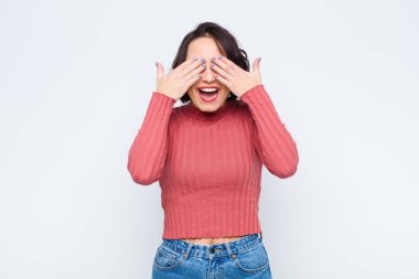 Genç ve güzel bir kadın gülümsüyor ve mutlu hissediyor, iki eliyle gözlerini kapatıyor ve beyaz duvara karşı inanılmaz bir sürpriz bekliyor.