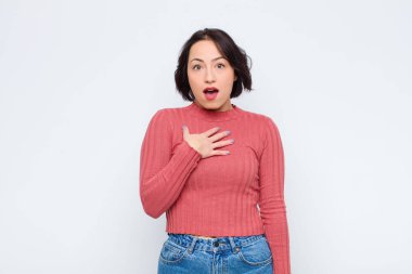 Genç, güzel bir kadın şok olmuş, şaşırmış ve şaşırmış hissediyor, elleri göğsünde ve ağzı açık, kim diyor, ben mi? Beyaz duvara yaslan