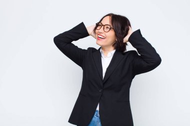 Genç iş kadını gülümsüyor ve rahat, tatmin olmuş ve kaygısız hissediyor, olumlu gülüyor ve beyaz duvara yaslanıyor.