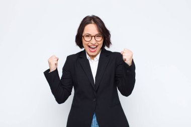 Genç iş kadını mutlu, pozitif ve başarılı hissediyor, zaferi, başarıları veya beyaz duvara karşı iyi şanslar diliyor.