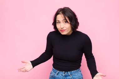 Genç, güzel bir kadın kendini cahil ve şaşkın hissediyor. Hiçbir fikri yok. Pembe duvara karşı aptal ya da aptal bir bakışla kafası karışmış.