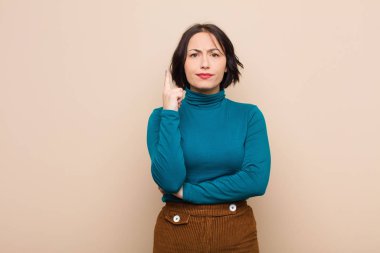 Genç ve güzel bir kadın, parlak bir fikri fark ettikten sonra parmağını havaya kaldırıp bej duvara karşı 