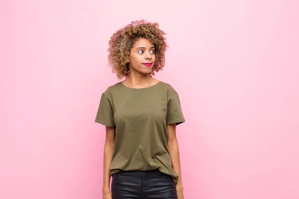 young african american woman wondering, thinking happy thoughts and ideas, daydreaming, looking to copy space on side against pink wall