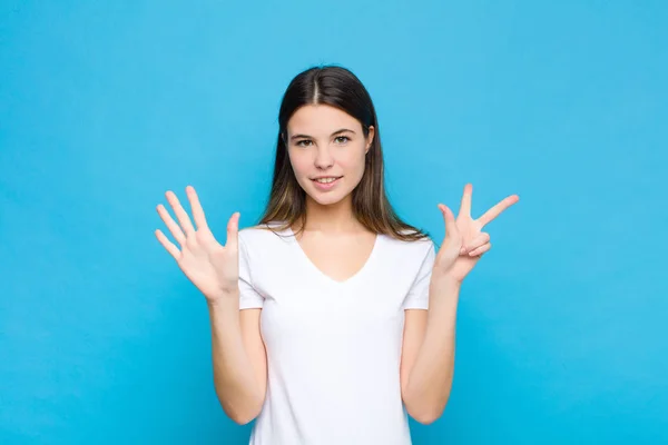 若い女性は笑顔で友好的です前方に手で8番目または8番目を示し青い壁に対してカウントダウン — ストック写真