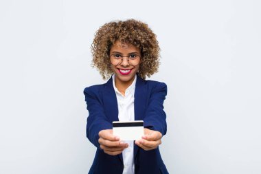 Genç Afrikalı Amerikalı kadın mutlu bir şekilde gülümsüyor, kendine güvenen, olumlu bakışlı, kredi kartıyla bir nesne ya da konsept sunuyor ve gösteriyor.