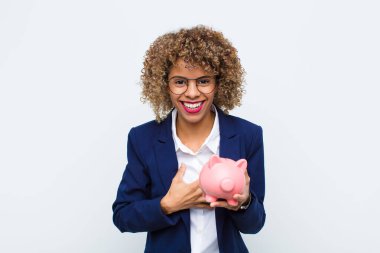 Genç Afrikalı Amerikalı bir kadın komik bir şakaya yüksek sesle gülüyor, mutlu ve neşeli hissediyor, domuz kumbarasıyla eğleniyor.