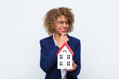 Genç Afrikalı Amerikalı kadın mutlu, kendine güvenen bir ifadeyle gülümsüyor. Çenesi çenesinde, merak ediyor ve ev modelinin tarafını tutuyor.