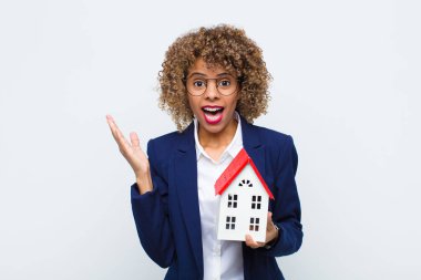 Genç Afrikalı Amerikalı kadın mutlu, heyecanlı, şaşırmış ya da şok olmuş hissediyor, gülümsüyor ve ev modeliyle ilgili inanılmaz bir şeye hayret ediyor.