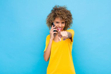 Genç Afrikalı Amerikalı tatmin olmuş, kendine güvenen, dost canlısı bir gülümsemeyle kameraya bakıyor ve seni cep telefonuyla seçiyor.