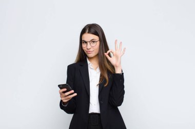 Genç, güzel bir kadın kendini mutlu, rahat ve tatmin olmuş hissediyor. Onayını iyi bir hareketle gösteriyor. Cep telefonuyla gülümsüyor.