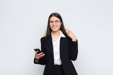 Genç, güzel bir kadın, kendine güvenerek gülümsüyor. Kendi gülüşünü gösteriyor. Pozitif, rahat, tatmin olmuş bir şekilde cep telefonuyla.