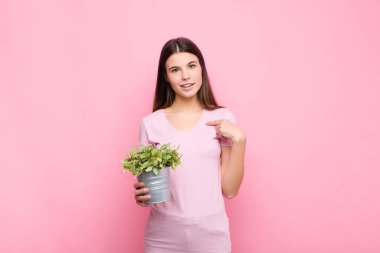 Genç, güzel bir kadın mutlu, şaşırmış ve gururlu hissediyor. Heyecanlı, şaşkın bakışlarıyla bir bitkiyi işaret ediyor.