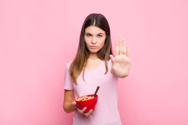 Genç ve güzel bir kadın ciddi, sert, hoşnutsuz ve kızgın görünüyor. Avuç içini açıp kahvaltılık kaseyle jestleri durduruyor.