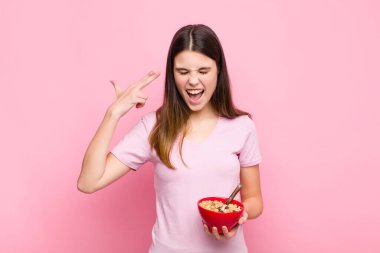 Genç ve güzel bir kadın mutsuz ve stresli görünüyor, intihar jesti silahla işaret ediyor, kafaya kahvaltı kasesi doğrultuyor.