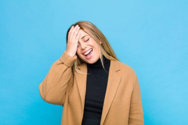 Genç sarışın kadın gülüyor ve alnına tokat atıyor. 