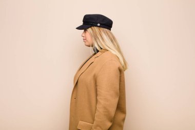 Profil görünümlü genç sarışın kadın önündekini kopyalamaya çalışıyor, düşünüyor, hayal ediyor ya da düz duvara karşı hayal kuruyor.