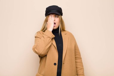 Genç sarışın kadın uykulu, sıkılmış ve esniyor, baş ağrısı ve yüzünün yarısını düz duvara dayamış.