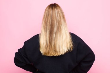 Genç sarışın kadın kafası karışık ya da dolgun hissediyor ya da şüphe ve sorular, merak ediyor, elleri kalçasında, düz duvara bakan dikiz aynası