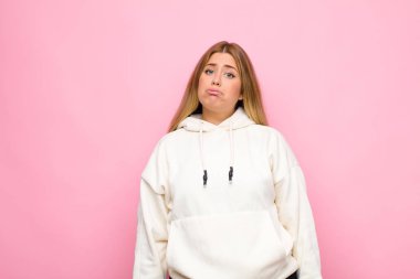 Genç sarışın kadın üzgün ve mızmız görünüyor. Mutsuz bir bakışla ağlıyor. Duvara karşı olumsuz ve hayal kırıklığına uğramış bir tavırla ağlıyor.