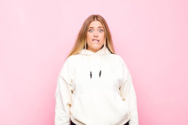 Genç sarışın kadın şaşkın ve şaşkın görünüyor, gergin bir hareketle dudağını ısırıyor, düz duvara karşı sorunun cevabını bilmiyor.