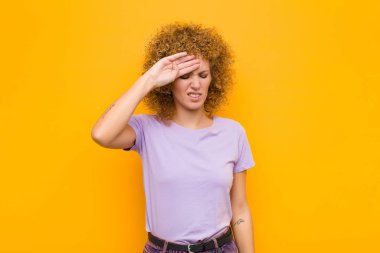 Genç afro kadın stresli, yorgun ve hayal kırıklığına uğramış görünüyor, alnından ter damlıyor, umutsuz ve turuncu duvarda bitkin hissediyor.