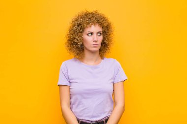 Genç afro kadın üzgün, üzgün ya da kızgın ve olumsuz bir tavır takınıyor, turuncu duvara karşı anlaşmazlık içinde.
