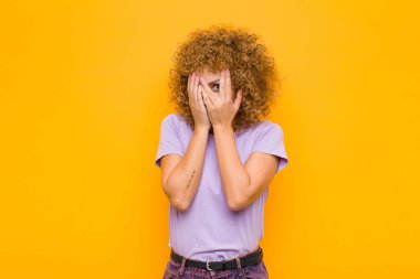 Genç afro kadın korkmuş ya da utanmış hissediyordu. Gözleri yarı kapalı turuncu duvara bakıyordu.