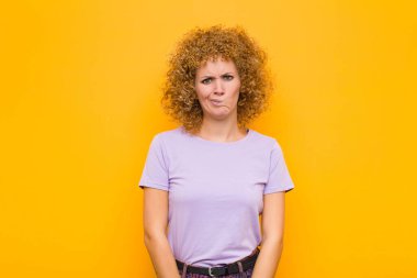 Genç afro kadın şaşkın ve kuşkulu hissediyor, merak ediyor ya da turuncu duvara karşı karar vermeye çalışıyor.