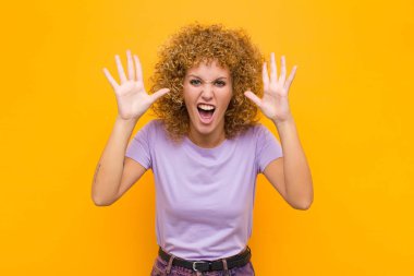 Panik ya da öfke içinde çığlık atan genç afro kadın, şok olmuş, korkmuş ya da öfkeli, elleri turuncu duvara dayalı.