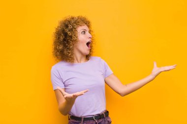 Genç afro kadın opera yapıyor veya konserde şarkı söylüyor, romantik, sanatsal ve turuncu duvara karşı tutkulu hissediyor.