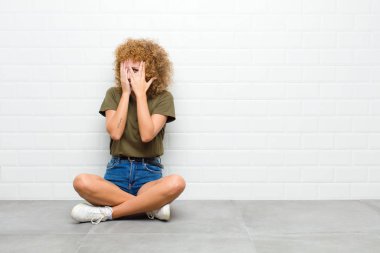 Genç afro kadın korkmuş ya da utanmış hissediyordu. Gözleri yarı kapalı, elleri yere oturmuş dikizliyordu.