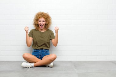 Genç afro kadın kendini mutlu, pozitif ve başarılı hissediyor, zaferi kutluyor, başarıları kutluyor ya da yerde otururken iyi şanslar diliyor.