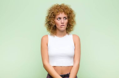 Genç afro kadın kuşkulanıyor ya da düşünüyor, dudağını ısırıyor ve gergin hissediyor, yeşil duvara karşı boşluğu kopyalamak istiyor.