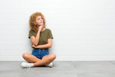 Genç afro kadın düşünceli, meraklı ya da hayal kuruyor, hayal kuruyor ve bir yerde oturmuş fotokopi çekmek için yukarı bakıyor.