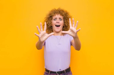 Genç afro kadın sersemlemiş ve korkmuş hissediyor, korkunç bir şeyden korkuyor, elleri açık turuncu duvardan uzak durun diyor.