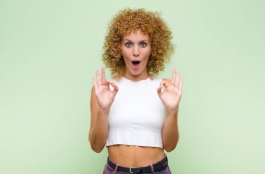 Genç afro kadın şok olmuş, şaşırmış ve şaşırmış hissediyor. Onaylıyor. İki elini de yeşil duvara dayayıp işaret veriyor.