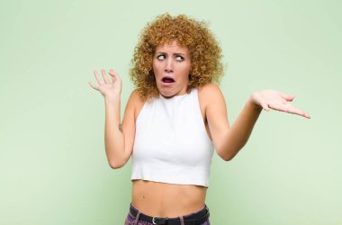 Genç afro kadın aptal, deli, şaşkın, şaşkın bir ifadeyle omuz silkiyor. Sinirli ve yeşil duvara karşı cahil hissediyor.