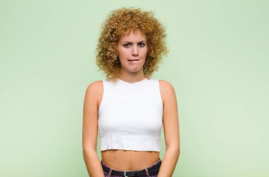 Genç afro kadın kendini cahil, kafası karışık ve hangi seçeneği seçeceği konusunda kararsız hissediyor, yeşil duvara karşı sorunu çözmeye çalışıyor.