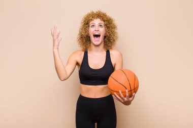 Genç afro kadın kendini mutlu, şaşkın, şanslı ve şaşırmış hissediyor. Zaferi iki elini de havaya kaldırarak kutluyor.